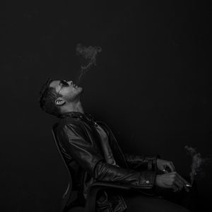 一位戴眼镜的年轻编辑坐在深色书桌前专注看着屏幕，桌面有绿色小台灯与便签纸，氛围安静